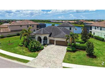 Stunning waterfront home featuring a tile roof, arched entryway, and lush tropical landscaping at 5622 Arnie Loop, Lakewood Ranch, FL 34211