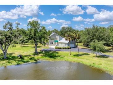 Charming home featuring a lush green lawn, mature trees, and a serene pond on a sunny day at 919 Palm View Way, Sarasota, FL 34240