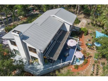 Stunning aerial view of the modern home, showcasing a metal roof, screened deck, manicured garden, and mature trees at 7251 Fish Farm Rd, Palmetto, FL 34221