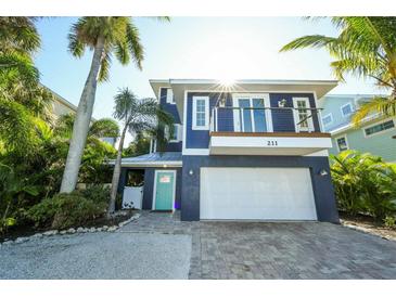 Two-story home with a blue facade, balcony, two car garage and lush, tropical landscaping at 211 65Th St, Holmes Beach, FL 34217