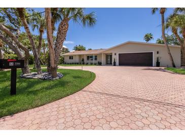 Beautiful single-story home with a circular brick paver driveway and a lush green lawn with palm trees at 5581 Shadow Lawn Dr, Sarasota, FL 34242