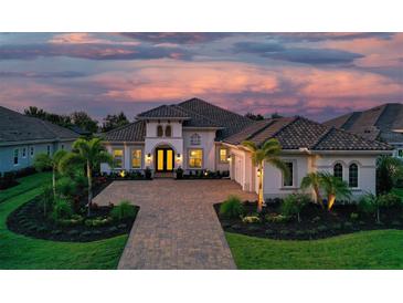 Elegant home with a brick paved driveway, manicured lawn, a two-car garage and lush landscaping at sunset at 7838 Bowspirit Way, Lakewood Ranch, FL 34202
