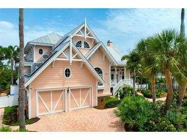 Charming two-story home featuring a brick driveway, multiple garage doors, and lush landscaping with palm trees at 512 77Th St, Holmes Beach, FL 34217