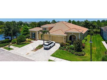 Stunning home featuring a tile roof, three-car garage, lush landscaping, and a brick driveway by a beautiful pond at 11603 Bluebird Pl, Lakewood Ranch, FL 34211