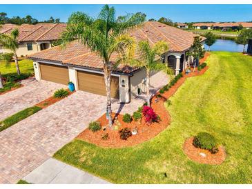 Beautiful home features a terracotta roof, two-car garage, paver driveway, tropical landscaping, and a lush green lawn at 12230 Amica Loop, Venice, FL 34293
