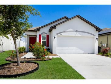 Charming one-story home with a well-manicured lawn, colorful flowers, and a bright red front door at 4739 Reisswood Loop, Palmetto, FL 34221
