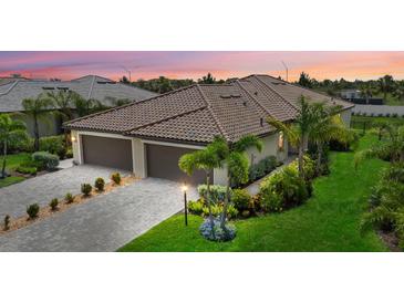 Beautifully landscaped exterior of home with three-car garage and brick driveway at sunset at 16012 Sunny Day Dr, Bradenton, FL 34211