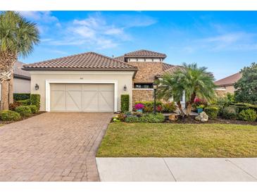 Charming single-story home featuring a tile roof, brick driveway, two-car garage, and lush landscaping at 5011 Tivoli Run, Bradenton, FL 34211