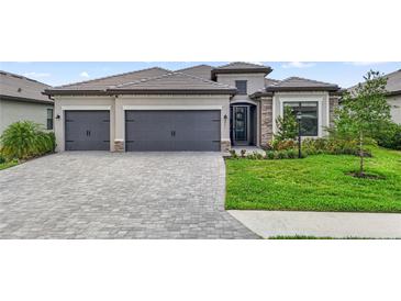 Charming home boasts a three-car garage, stone accents, tile roof, lush landscaping, and a brick paver driveway at 4971 Oyster Pearl St, Bradenton, FL 34211
