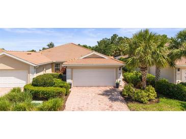 Charming home featuring a tile roof, brick driveway, and well-maintained landscaping with vibrant greenery and a mature palm tree at 5866 Guarino Dr, Sarasota, FL 34238