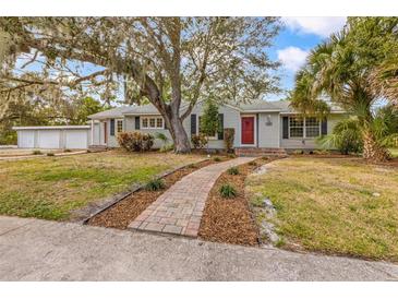 Charming single-story home featuring a well-manicured lawn, mature trees, and a welcoming red front door at 102 28Th W St, Bradenton, FL 34205