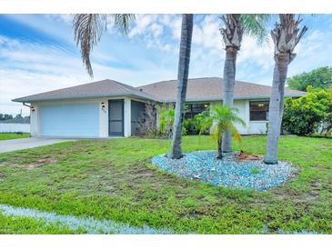 Charming single-story home with a two-car garage, lush green lawn, and mature palm trees at 408 Fletcher St, Port Charlotte, FL 33954