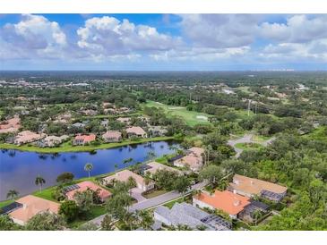 Stunning aerial view of a golf course community featuring a scenic pond, lush greenery, and beautiful homes with tile roofs at 7214 Marlow Pl, University Park, FL 34201