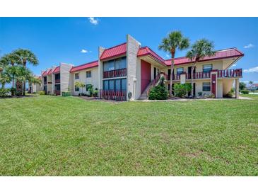 Low angle exterior of a multi-Gathering home with lush green grass, palm trees, and a red roof at 96 Boundary Blvd # 127, Rotonda West, FL 33947