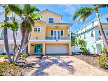 Charming yellow two-story home with balcony, turquoise door, brick driveway, and palm trees at 145 50Th St, Holmes Beach, FL 34217