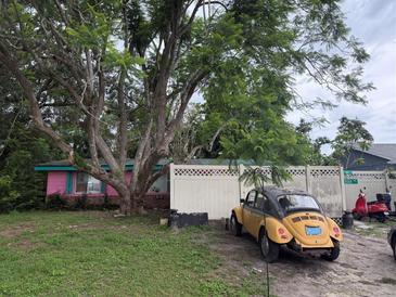 Whimsical cottage-style home with pink accents, mature trees, and a vintage car parked in front at 5011 Elfrida Ave, Sarasota, FL 34235