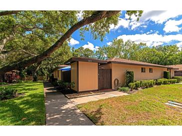 Inviting tan home with manicured lawn, decorative landscaping, and mature shade tree in a quiet neighborhood at 8472 60Th N St # 702, Pinellas Park, FL 33781
