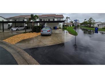 Exterior of condo featuring covered parking, landscaping, and street view on a rainy day at 1211 Capri Isles Blvd # 116, Venice, FL 34292