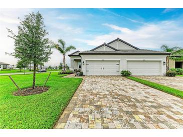 Charming two-story home showcasing a three-car garage, brick driveway, and beautifully landscaped front yard at 17898 Cherished Loop, Bradenton, FL 34211