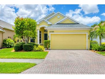 Charming yellow single-story home with a well-manicured lawn and brick driveway, showcasing curb appeal at 2085 Mattamy Ct, Venice, FL 34292
