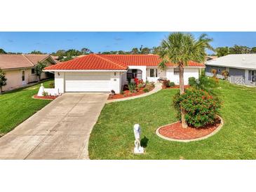 Charming single-story home featuring a red tile roof, a well-manicured lawn, and lush tropical landscaping at 74 Windsor Dr, Englewood, FL 34223