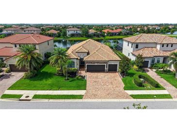 Beautiful tile roof home with a brick driveway, two car garage, and manicured green lawn with palm trees at 13220 Swiftwater Way, Lakewood Ranch, FL 34211