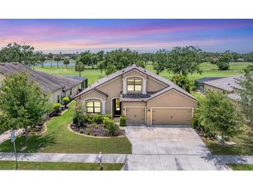 Charming tan house with a three-car garage, manicured lawn, and landscaping on a golf course at 9123 Raes Creek Pl, Palmetto, FL 34221