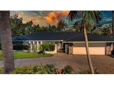 Charming single-story home featuring a black roof, stone accents, paved driveway, and lush landscaping at 483 Partridge Cir, Sarasota, FL 34236