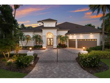 Elegant single-story home featuring a gated entrance, arched entryway, two-car garage, and lush tropical landscaping at dusk at 7211 Pasadena Gln, Lakewood Ranch, FL 34202