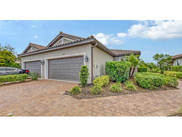 Home exterior featuring a two-car garage, brick driveway, beautiful landscaping, and tile roof at 10254 Morning Mist Ln, Sarasota, FL 34241