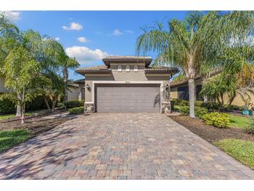 Charming home featuring a paver driveway and two-car garage, complemented by lush palm trees and well-maintained landscaping at 19023 Mangieri St, Venice, FL 34293