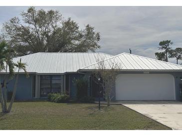 Charming single-story home with a lush lawn, a metal roof, mature landscaping, and an attached garage at 22321 Yonkers Ave, Port Charlotte, FL 33952