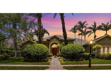 Stunning home exterior with lush landscaping, palm trees, and a beautiful walkway to the front door at sunset at 8999 Wildlife Loop, Sarasota, FL 34238