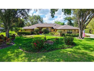 Beautifully landscaped front yard of tan single-story home with mature trees, lush lawn and manicured flower beds at 7426 Weeping Willow Blvd, Sarasota, FL 34241