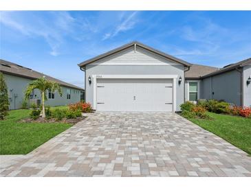 Exterior view of a home featuring a two-car garage, brick paver driveway, and well-maintained landscaping at 9566 Coastline Way, Parrish, FL 34219