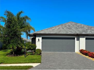 Exterior view of a well-kept home featuring a grey two car garage, pavers, manicured lawn, and vibrant landscaping at 16087 Sunny Day Dr, Bradenton, FL 34211