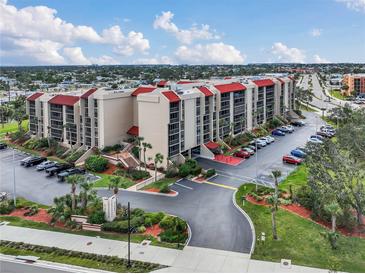 Stunning exterior view of a condominium complex with a red roof, lush landscaping and ample parking at 21405 Olean Blvd # 224, Port Charlotte, FL 33952
