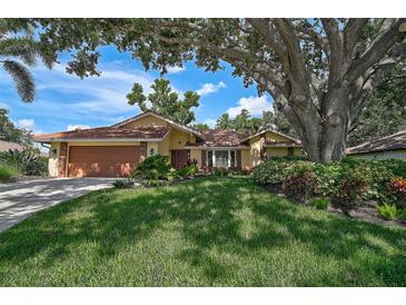 Charming single-story home featuring a terracotta tile roof, beautiful landscaping, and a large shade tree at 1674 Cottonwood Trl, Sarasota, FL 34232