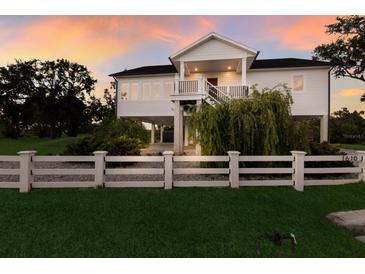 Charming two-story waterfront home featuring a white picket fence, lush landscaping, and elevated construction at 1610 Bayshore Dr, Terra Ceia, FL 34250