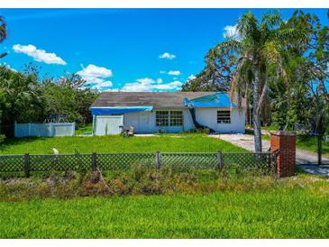 Exterior of home featuring a small yard, mature landscaping, and damage to roof covered by tarp at 1230 Bayshore Dr, Terra Ceia, FL 34250