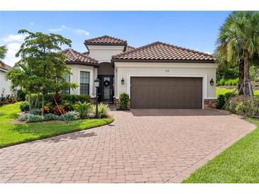 Charming single-story home with a red tile roof, brown garage door, brick driveway, and lush landscaping at 4735 Cassio Ct, Bradenton, FL 34211