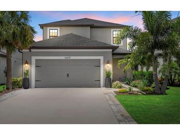 Two-story gray home featuring a gray garage door, tropical landscaping, and a paver driveway at 16419 Paynes Mill Dr, Bradenton, FL 34211