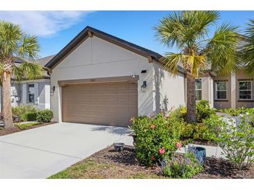 Home exterior showing a two-car garage and a landscaped yard with flowering bushes and palm trees at 5981 Amberly Dr, Bradenton, FL 34208