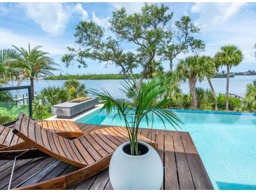 Stunning waterfront pool featuring a sun deck with lounge chairs overlooking the calm waters and blue skies at 4907 Topsail Dr, Nokomis, FL 34275