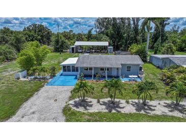 Charming home with a blue painted driveway, manicured lawn, lush landscaping, and a detached garage at 27437 Dutch Ave, Punta Gorda, FL 33982