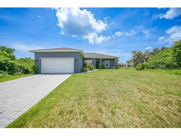 Charming single-story home with a gray exterior, white garage door, and landscaped yard at 725 Essex Ave, Port Charlotte, FL 33948