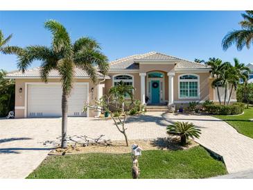 Tan single-Gathering home with a teal door, two-car garage, and paver driveway at 1310 Monte Carlo Ct, Punta Gorda, FL 33950