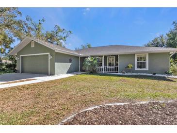 Green house exterior with a two-car garage and a spacious front yard at 1811 Music Ln, North Port, FL 34286