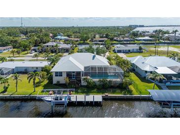 Back of waterfront home featuring a screened-in pool, boat dock, and well-maintained lawn with palm trees at 4431 Gardner Dr, Port Charlotte, FL 33952