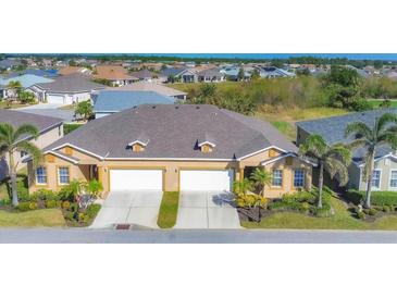 Aerial view of a tan two-car garage villa with a grey roof, surrounded by lush landscaping and other homes at 1916 Nottingham Trl, Punta Gorda, FL 33980